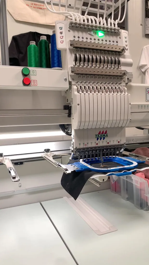 Machine à broder de l’atelier en train de réaliser un logo sur du simili noir tendu dans un cadre