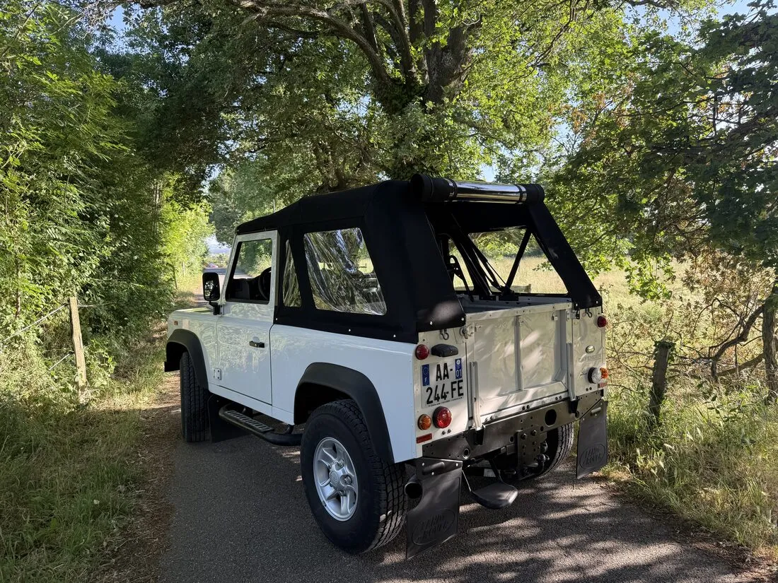 Land Rover Defender X-trem avec sa capote sur mesure neuve, vu de trois quarts sur une route de campagne