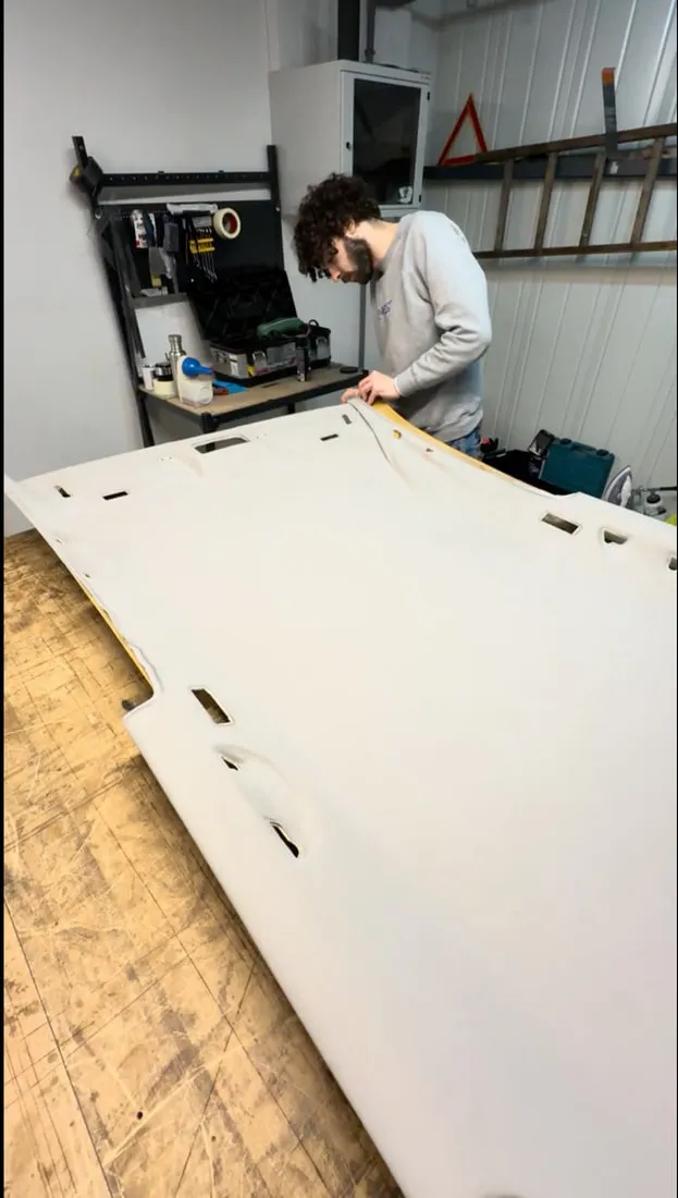 Pose du tissu neuf sur la coque de ciel de toit posée à plat sur l’établi de l’atelier