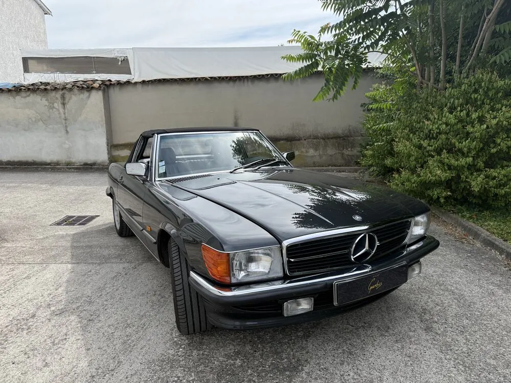 Mercedes SL R107 noire garée devant l’atelier, capote fermée