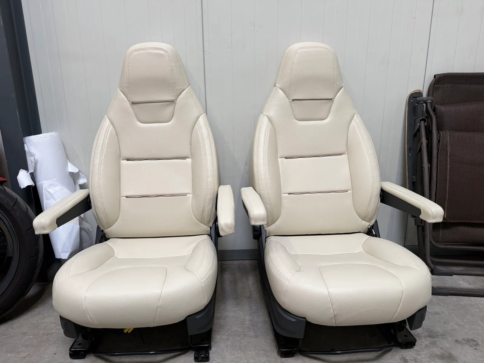 Deux sièges avant de camping-car Fiat Ducato refaits en simili beige, debout dans l’atelier