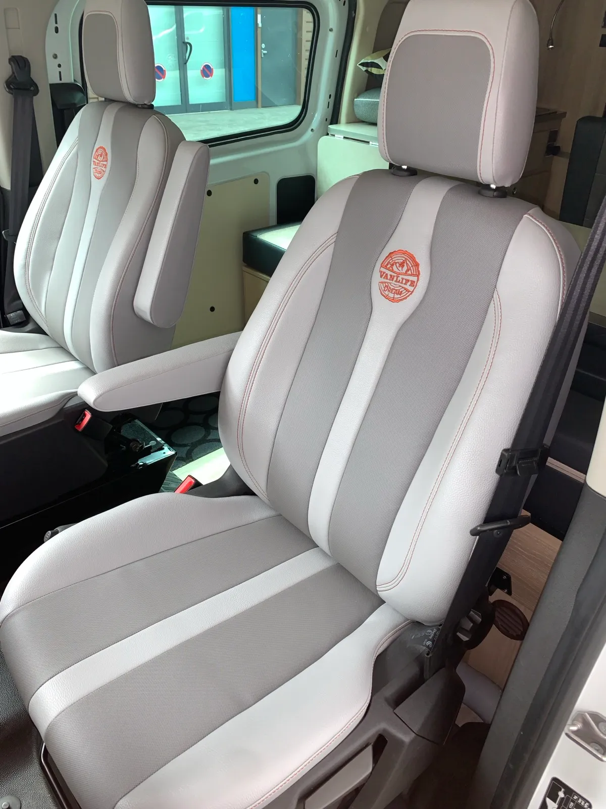 Sièges avant d’un Ford Transit aménagé refaits en simili bi-ton gris et blanc, avec surpiqûres orange et logo brodé
